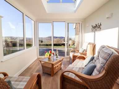 A sunroom with wicker furniture and a coffee table with flowers and drinks at Berwyn View in Trelydan near Welshpool
