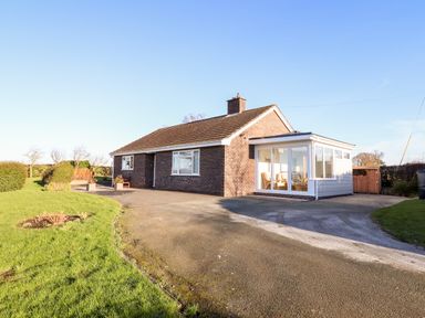 A brick bungalow with a driveway and a glass sunroom at Berwyn View in Trelydan near Welshpool