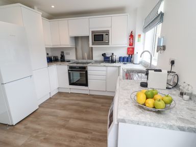 A kitchen with white cabinets a refrigerator oven microwave fruit bowl and sink at Beach Cottage in Portreath