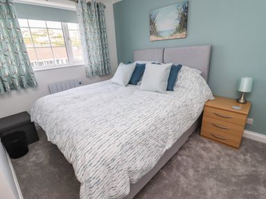 A bedroom with a bed with patterned bedding pillows bedside table with lamp and window with curtains at Beach Cottage in Portreath
