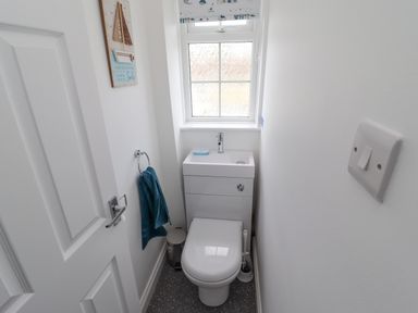 A small bathroom with a toilet and a small sink under a window with a towel hanging on the wall at Beach Cottage in Portreath
