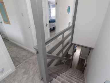 A carpeted staircase with grey railing leading down to a wooden floor hallway with doors and a carpeted upstairs hallway with white walls at Beach Cottage in Portreath