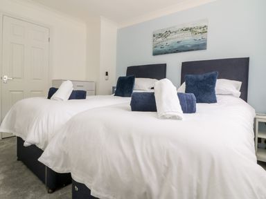A bedroom with two single beds with white bedding and blue pillows with towels on the beds at Beach Cottage in Portreath