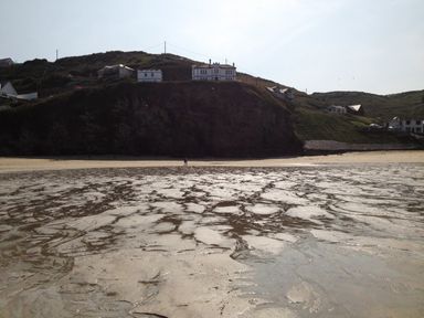 A sandy beach with wet sand patterns below cliffs with houses on top at Beach Cottage in Portreath