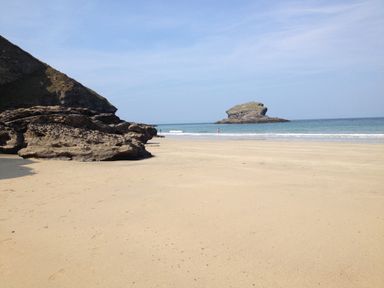 A sandy beach with rocks on the left and a rock formation in the water at Beach Cottage in Portreath