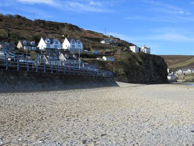A sandy beach with a stone sea wall and houses on a hillside at Beach Cottage in Portreath