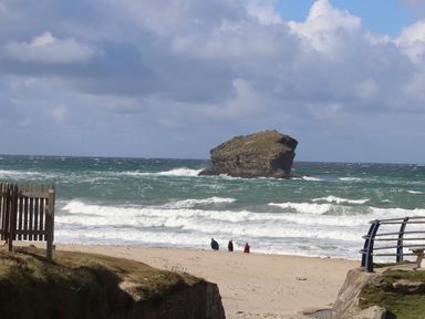 A beach with three people near the water and a large rock formation in the sea at Beach Cottage in Portreath