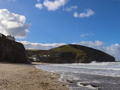 A sandy beach with waves and houses on cliffs and hills at Beach Cottage in Portreath