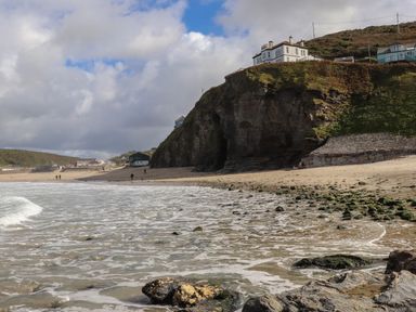 A sandy beach with a rocky cliff and houses on top at Beach Cottage in Portreath