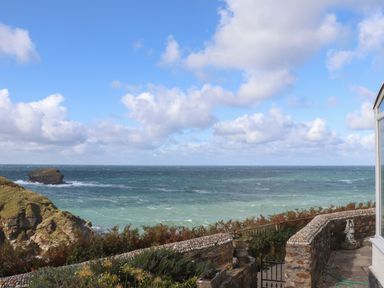 A stone patio and garden overlooking the ocean with a small rocky island and partly cloudy sky at Beach Cottage in Portreath