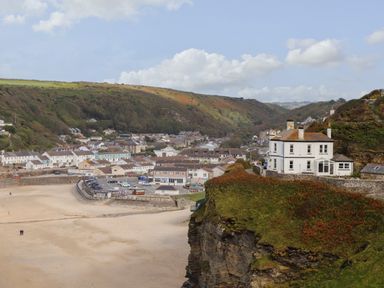 A coastal village with houses near a sandy beach and a large white house on a cliff at Beach Cottage in Portreath