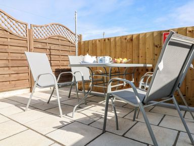 An outdoor patio with four chairs and a table with a teapot cups and fruit bowl at Beach Cottage in Portreath