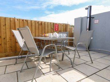 An outdoor patio area with a table and four chairs a fruit bowl teapot mugs and a shower on the wall at Beach Cottage in Portreath