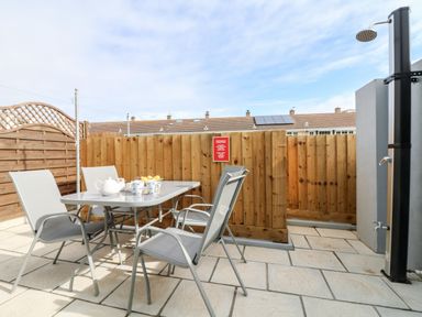 A patio with a table and four chairs teapot and cups on table outdoor shower and wooden fence at Beach Cottage in Portreath