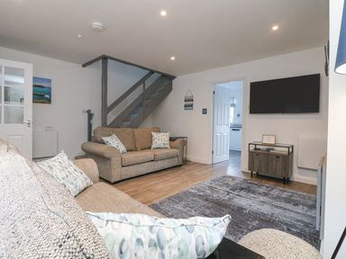 A living room with two sofas a staircase a wall-mounted television and a door leading to a kitchen at Beach Cottage in Portreath