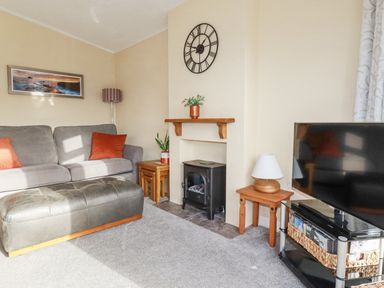 A living room with a grey sofa orange cushions a black ottoman and a television at Laurel Lodge Bossiney Bay Holiday Park near Tintagel