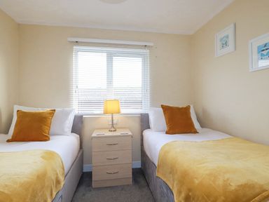 A bedroom with two single beds separated by a small bedside table holding a lamp at Laurel Lodge Bossiney Bay Holiday Park near Tintagel