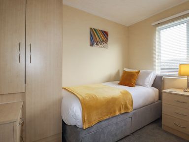A bedroom with a single bed a wardrobe a chest of drawers a window with blinds and a lamp at Laurel Lodge Bossiney Bay Holiday Park near Tintagel