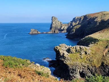 A coastal cliff landscape with rocky formations and blue ocean water at Laurel Lodge Bossiney Bay Holiday Park near Tintagel