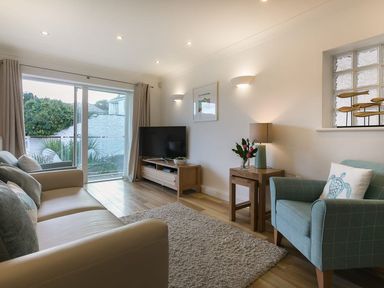 A living room with a beige sofa blue armchair wooden TV stand and sliding glass door at Atlantis in St Ives