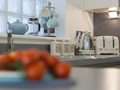 A kitchen countertop with a blue teapot a French press blue polka dot mugs on a stand labeled jars a silver electric kettle and a white toaster at Atlantis in St Ives