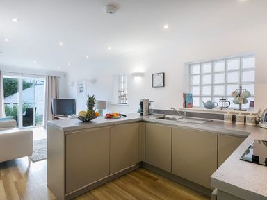 A kitchen with a fruit bowl on the counter and a living area with a TV and sliding glass door at Atlantis in St Ives