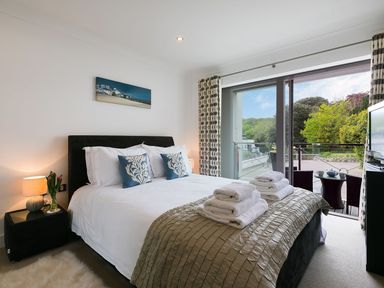 A bedroom with a bed two blue pillows bedside table lamp and patio doors overlooking a balcony at Atlantis in St Ives