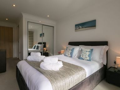 A bedroom with a bed with blue and white pillows and rolled white towels on a beige runner at Atlantis in St Ives