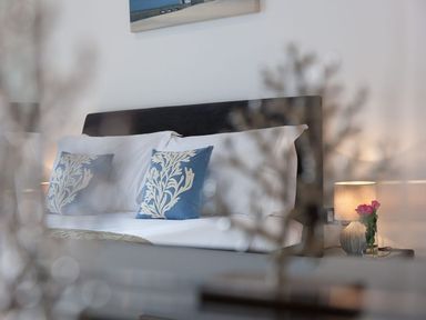 A bedroom with a bed with blue and white pillows and a bedside table with a lamp and flowers at Atlantis in St Ives