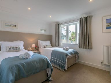 A bedroom with two single beds with blue throws and pillows next to a window with curtains at Atlantis in St Ives