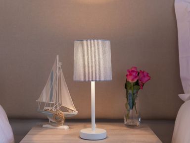 A bedside table with a model sailboat a lamp with a striped shade and a glass vase with pink roses at Atlantis in St Ives