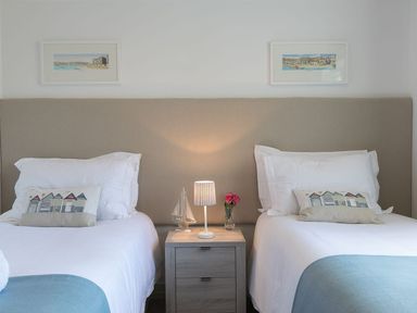A bedroom with two single beds a bedside table lamp and small sailboat at Atlantis in St Ives