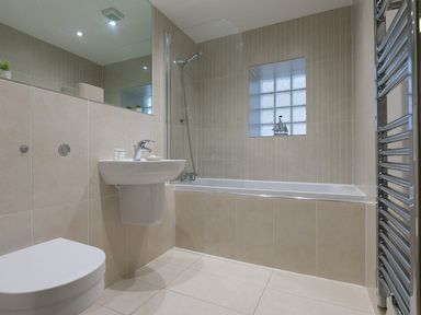 A bathroom with a bathtub shower combination sink toilet tiled walls and a towel radiator at Atlantis in St Ives