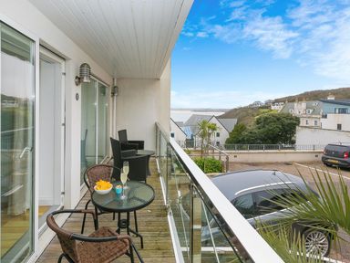 A balcony with a table and chairs overlooking a parking area and nearby houses at Atlantis in St Ives
