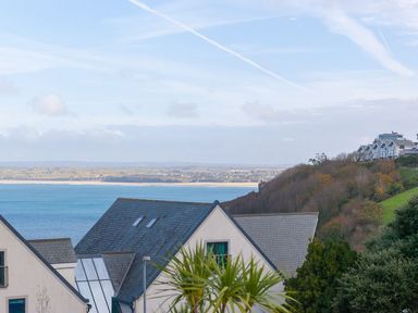 A coastal view with rooftops of houses foreground and hills with more buildings in the background at Atlantis in St Ives