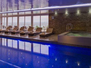 An indoor swimming pool with lounge chairs and a hot tub by a stone wall at Atlantis in St Ives