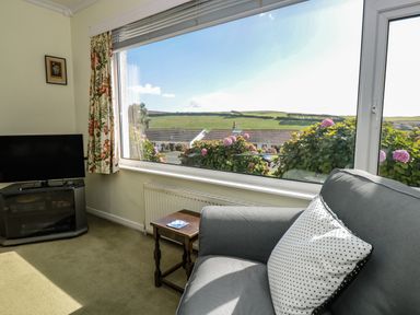 A sitting area with a gray armchair and polka dot pillow next to a window with floral curtains and a TV on a stand at 33 Weymouth Park in Hope Cove