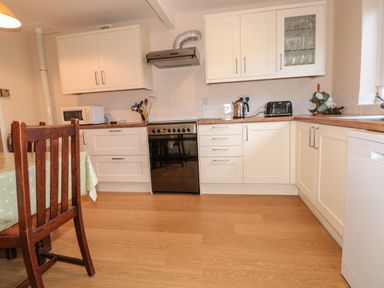 A kitchen with white cabinets wooden countertops a stove microwave kettle toaster and a wooden chair at 33 Weymouth Park in Hope Cove