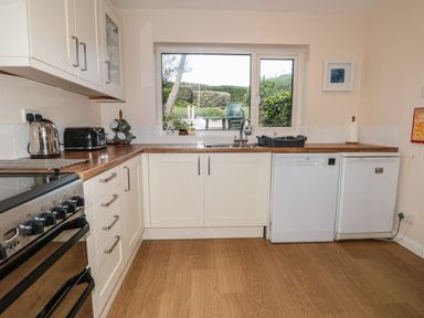 A kitchen with white cabinets wooden countertops a stove a toaster a kettle a sink and a window showing outdoor greenery at 33 Weymouth Park in Hope Cove