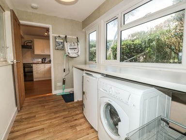 A utility room with a washing machine fridge mop and large windows at 33 Weymouth Park in Hope Cove