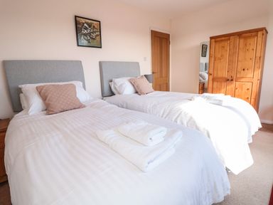 A bedroom with two single beds with white bedding and towels a wooden wardrobe a door and a framed picture on the wall at 33 Weymouth Park in Hope Cove