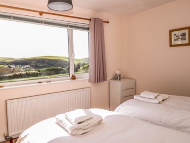 A bedroom with two beds towels on beds a window with a view and a small white dresser at 33 Weymouth Park in Hope Cove