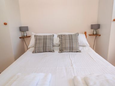 A bed with two plaid pillows two lamps on wall shelves and folded towels on the bed at 33 Weymouth Park in Hope Cove