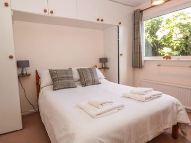 A bedroom with a double bed with pillows and folded towels under a window with curtains at 33 Weymouth Park in Hope Cove