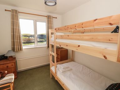 A bedroom with wooden bunk beds a wooden chair and a window showing a landscape at 33 Weymouth Park in Hope Cove
