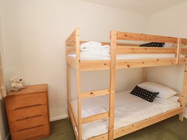 A bedroom with a wooden bunk bed with white bedding a wooden chest of drawers and a teddy bear on top at 33 Weymouth Park in Hope Cove