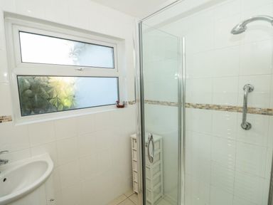 A bathroom with a sink a frosted window a glass shower enclosure and a storage unit at 33 Weymouth Park in Hope Cove