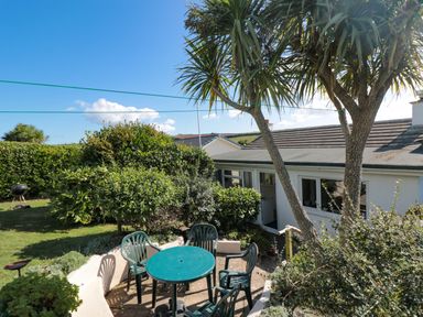 A garden patio with a round table and chairs surrounded by bushes and trees at 33 Weymouth Park in Hope Cove