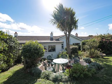 A garden patio area with a round table and four chairs surrounded by plants and a tree at 33 Weymouth Park in Hope Cove