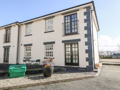 The exterior view of a two story building with black framed windows and doors with a small outdoor seating area and flower pot at Harbour View in Porthmadog